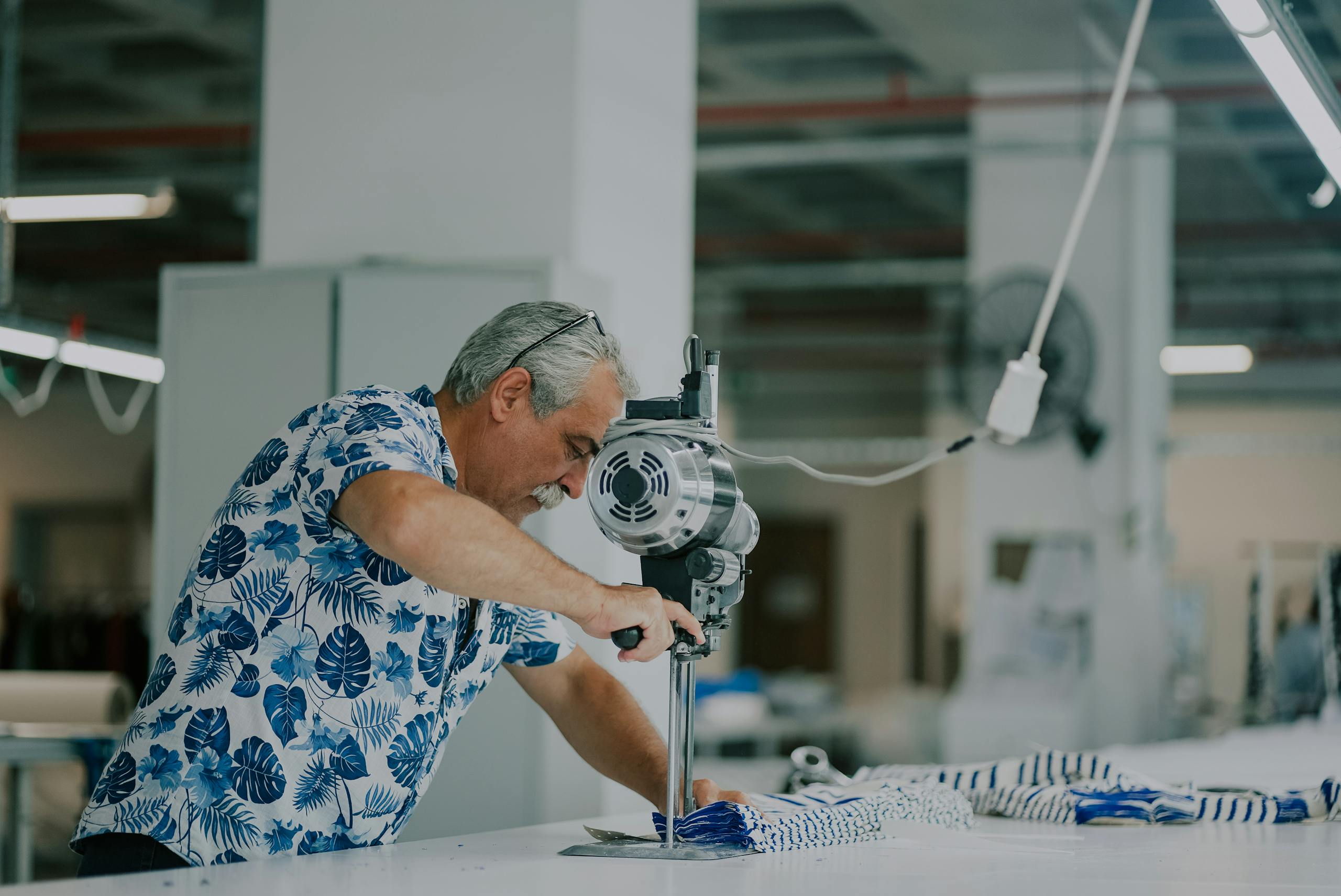 An adult man operates industrial machinery in a textile workshop, focusing on precision.